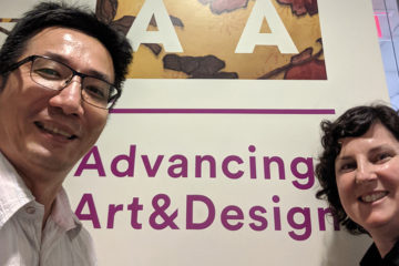 CJ Yeh and Austin Thomas post in front of CAA poster