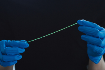 Gloved hands holding a green fiber