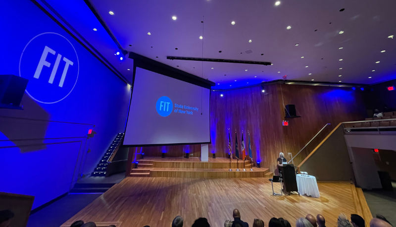 Interim Vice President for Academic Affairs Yasemin Jones on stage at a podium with screen behind her with projected FIT logo