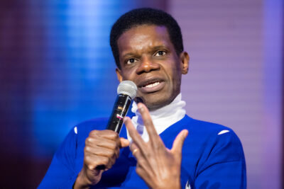 Closeup of Victor Glemaud in a blue sweater speaking into a microphone