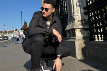 Student crouching down on the pavement with the London Tower behind him.